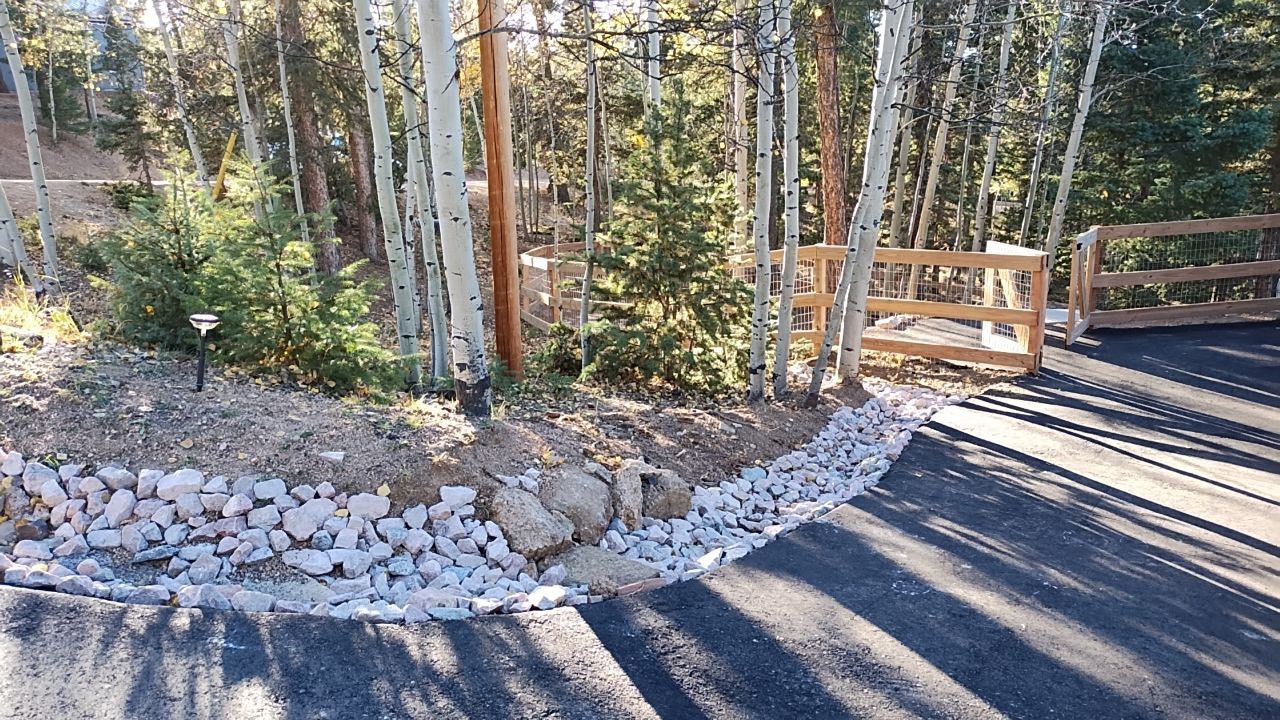 A wooden fence is surrounded by trees and rocks on the side of a road.