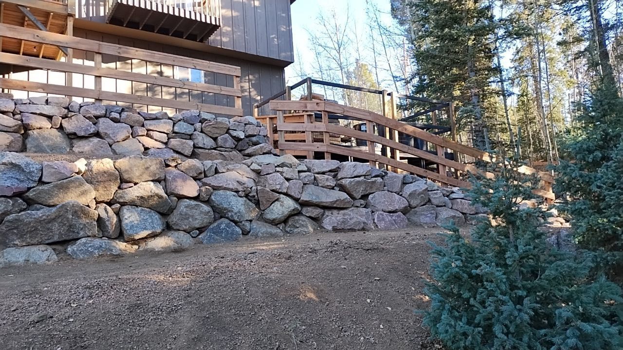 A stone wall with a wooden fence in front of a house.