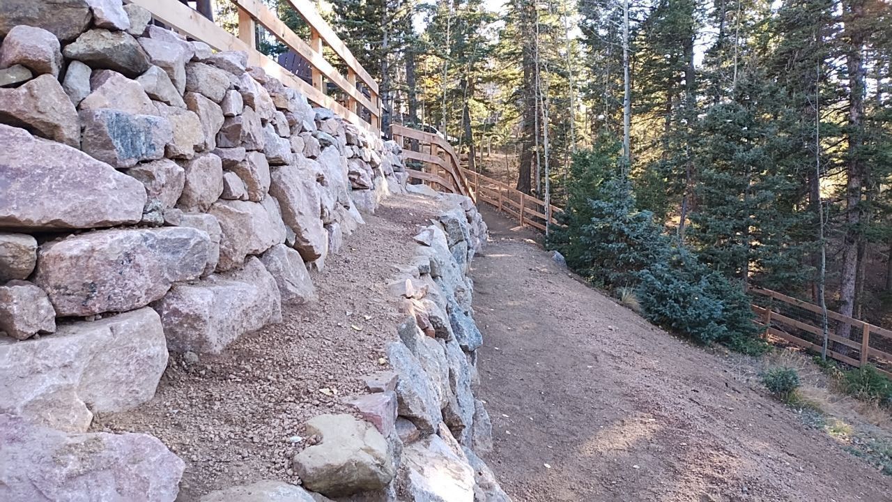 A stone wall surrounds a dirt path in the woods.