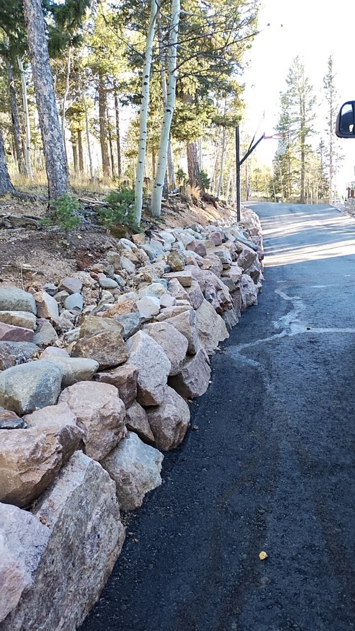 A stone wall along the side of a road with trees in the background.