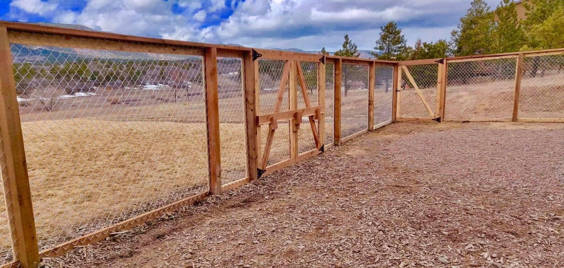 A wooden fence surrounds a gravel area in a field.
