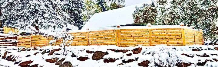 A wooden fence is covered in snow in the woods.