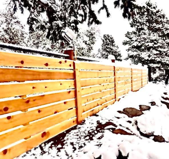 A wooden fence in the snow with trees in the background