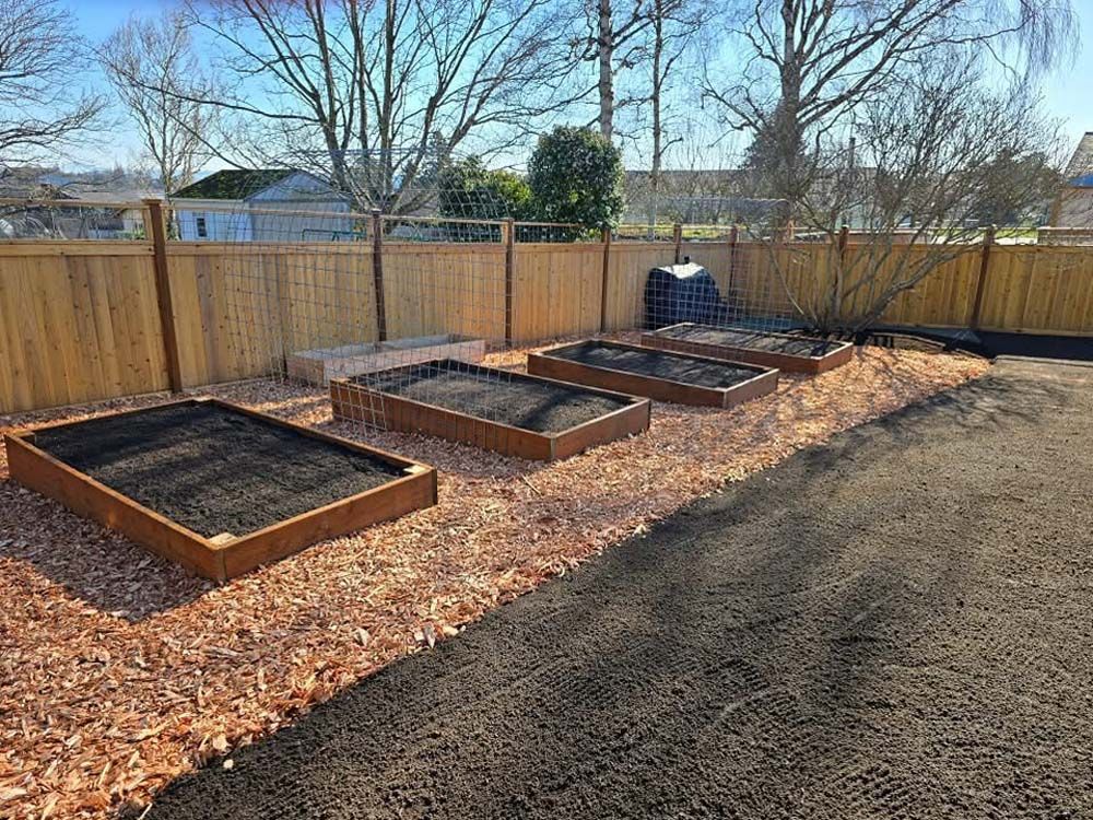Four rectangular raised garden beds with dark soil, surrounded by wood chips, next to a wood fence.