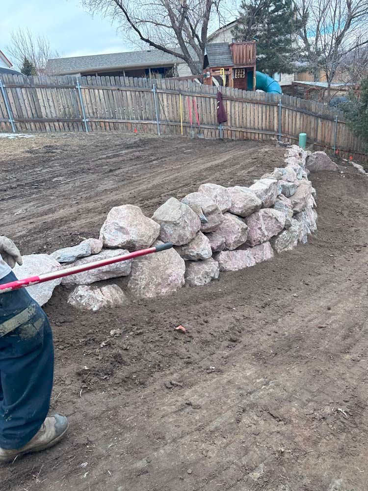Person building a retaining wall with large rocks in a backyard.