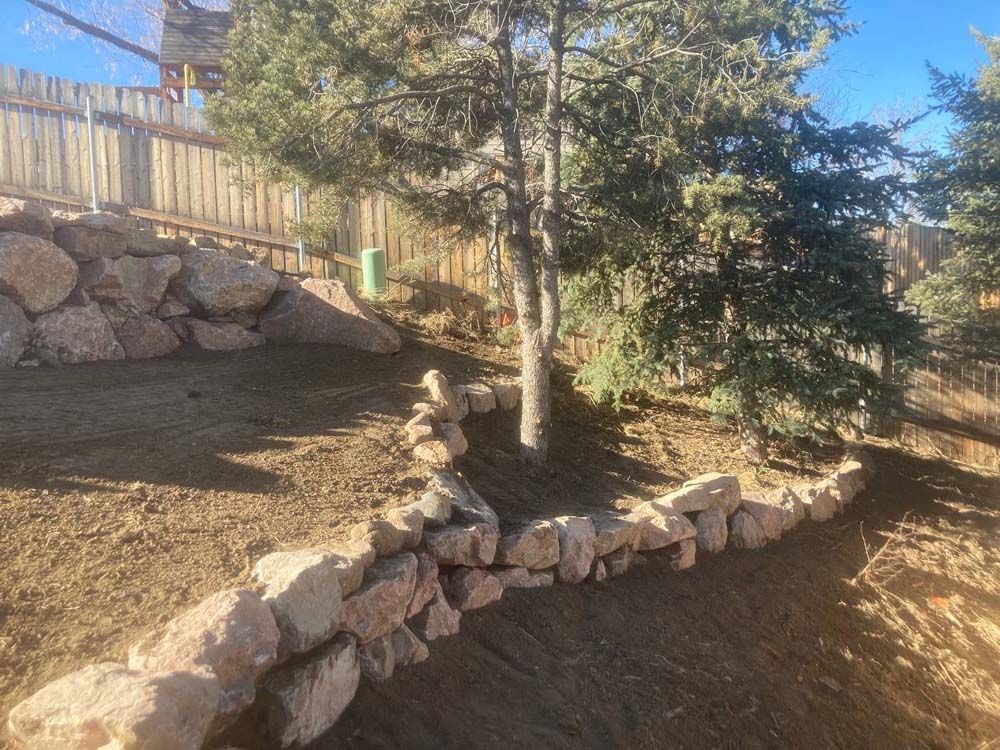 Stone retaining walls on a hillside with trees and a wooden fence.