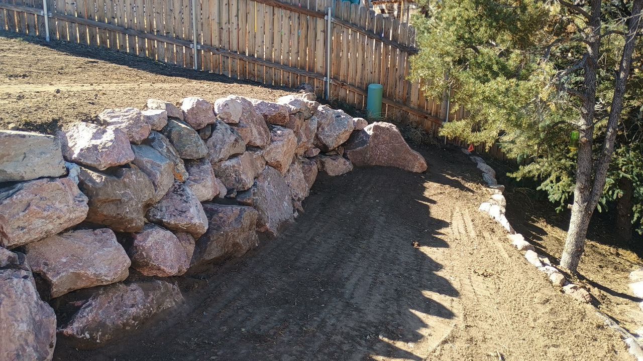 A pile of rocks sits in the dirt next to a wooden fence