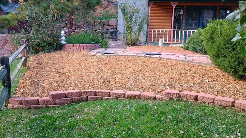 A front yard with a gravel bed, brick borders, and a path leading to a cabin-style house.