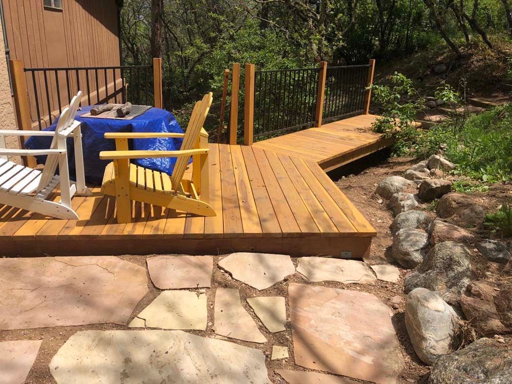 Wooden deck with Adirondack chairs, stone patio, and black railing.