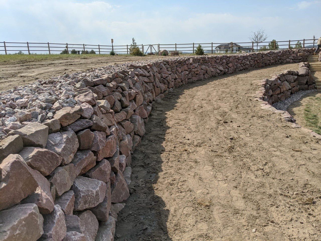 A stone wall surrounds a dirt path in a field