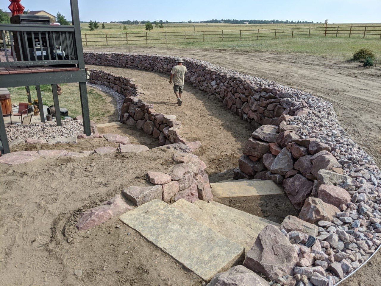 A man is walking along a stone wall in a field.
