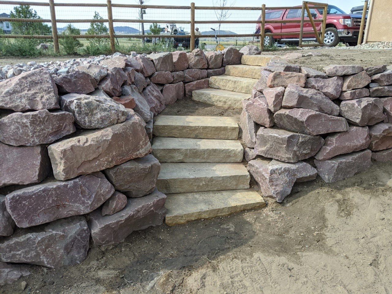 A red truck is parked behind a stone wall with stairs leading up to it.