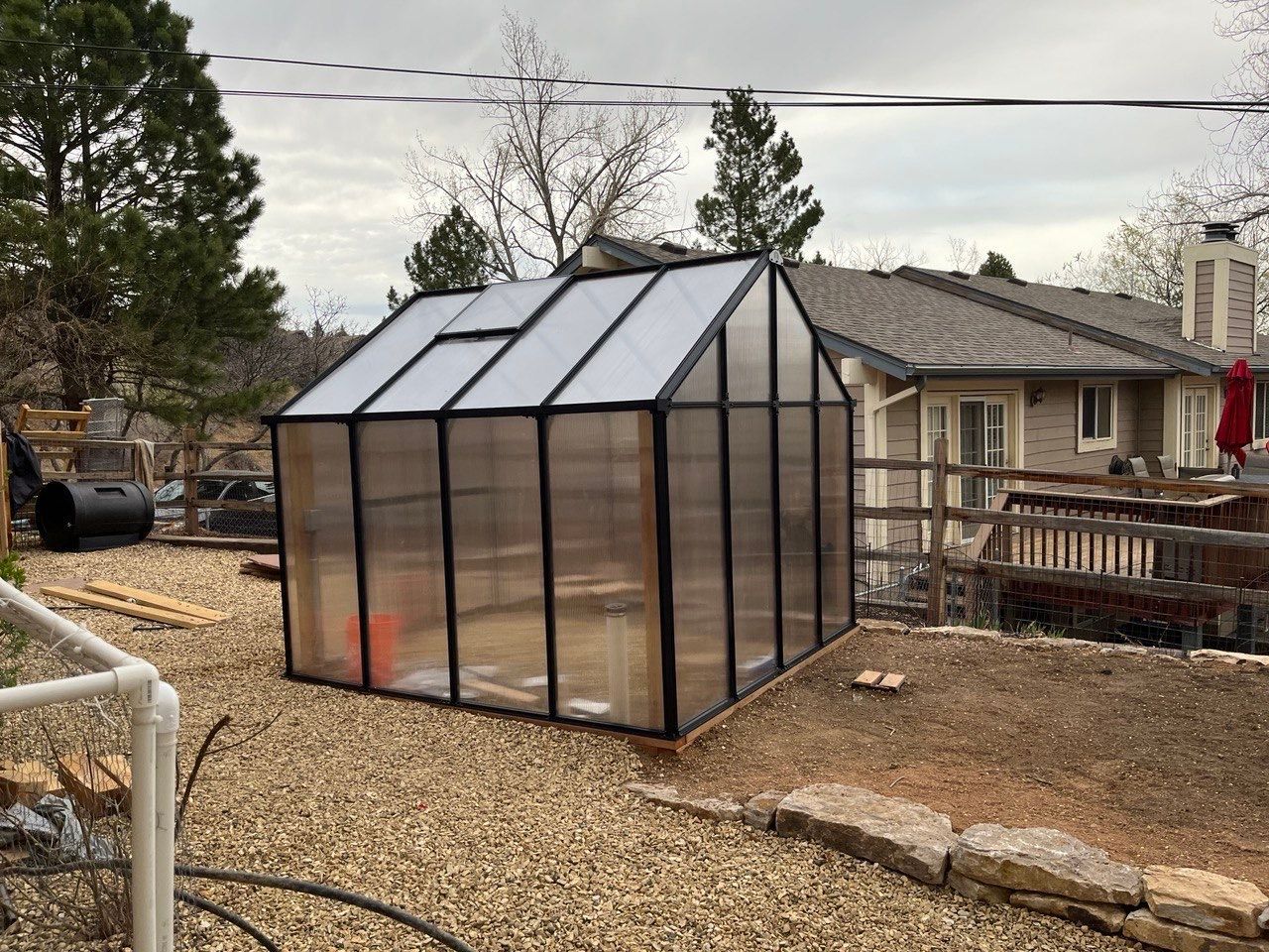 A greenhouse is sitting in the dirt in front of a house.