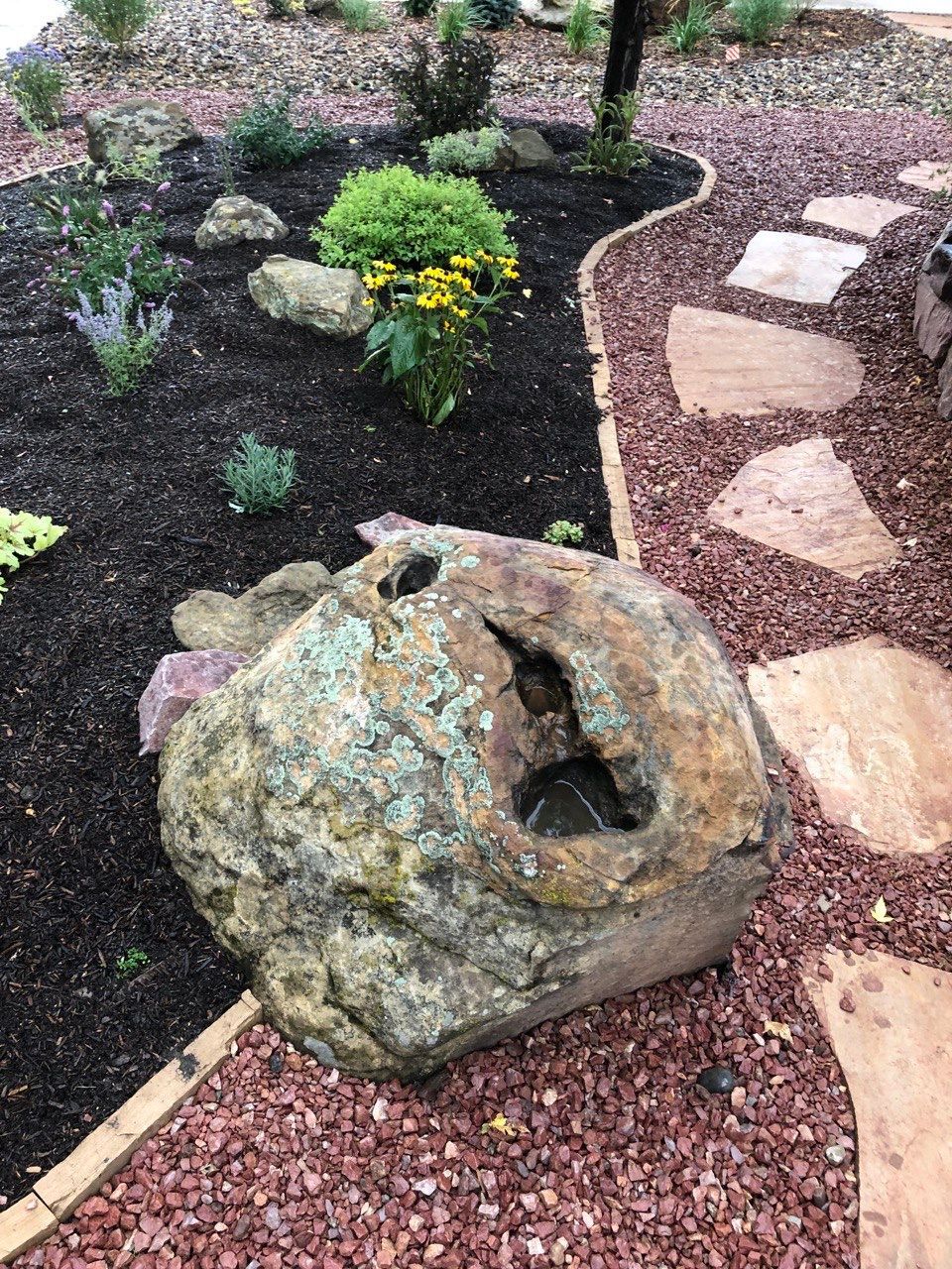 A large rock is sitting in the middle of a garden.