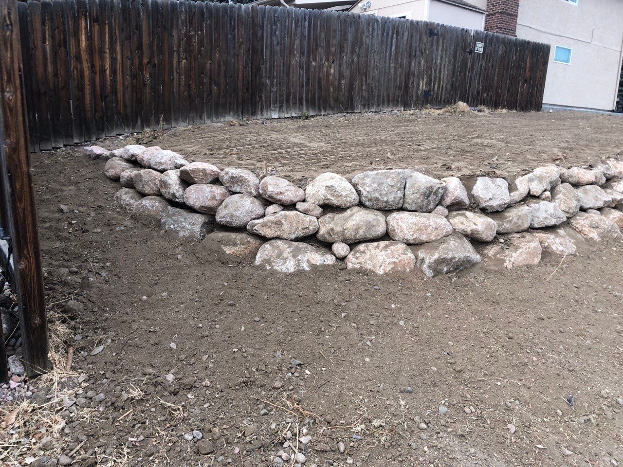 A pile of rocks sits in the dirt in front of a wooden fence