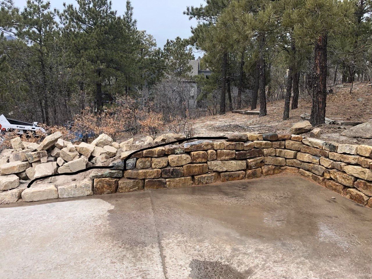 A stone wall is surrounded by trees on a hillside.