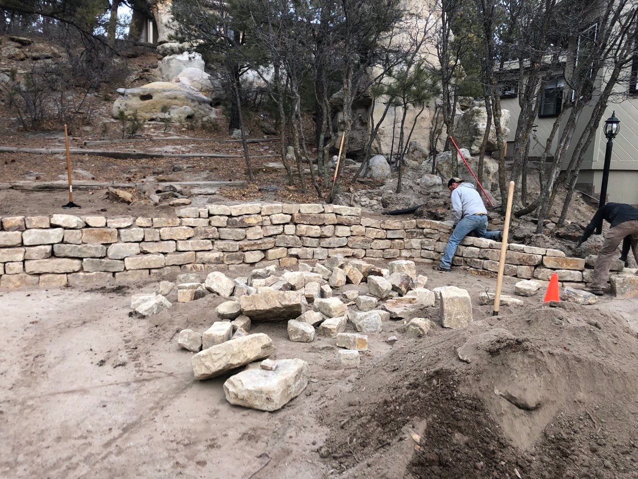 A man is working on a stone wall in the dirt.