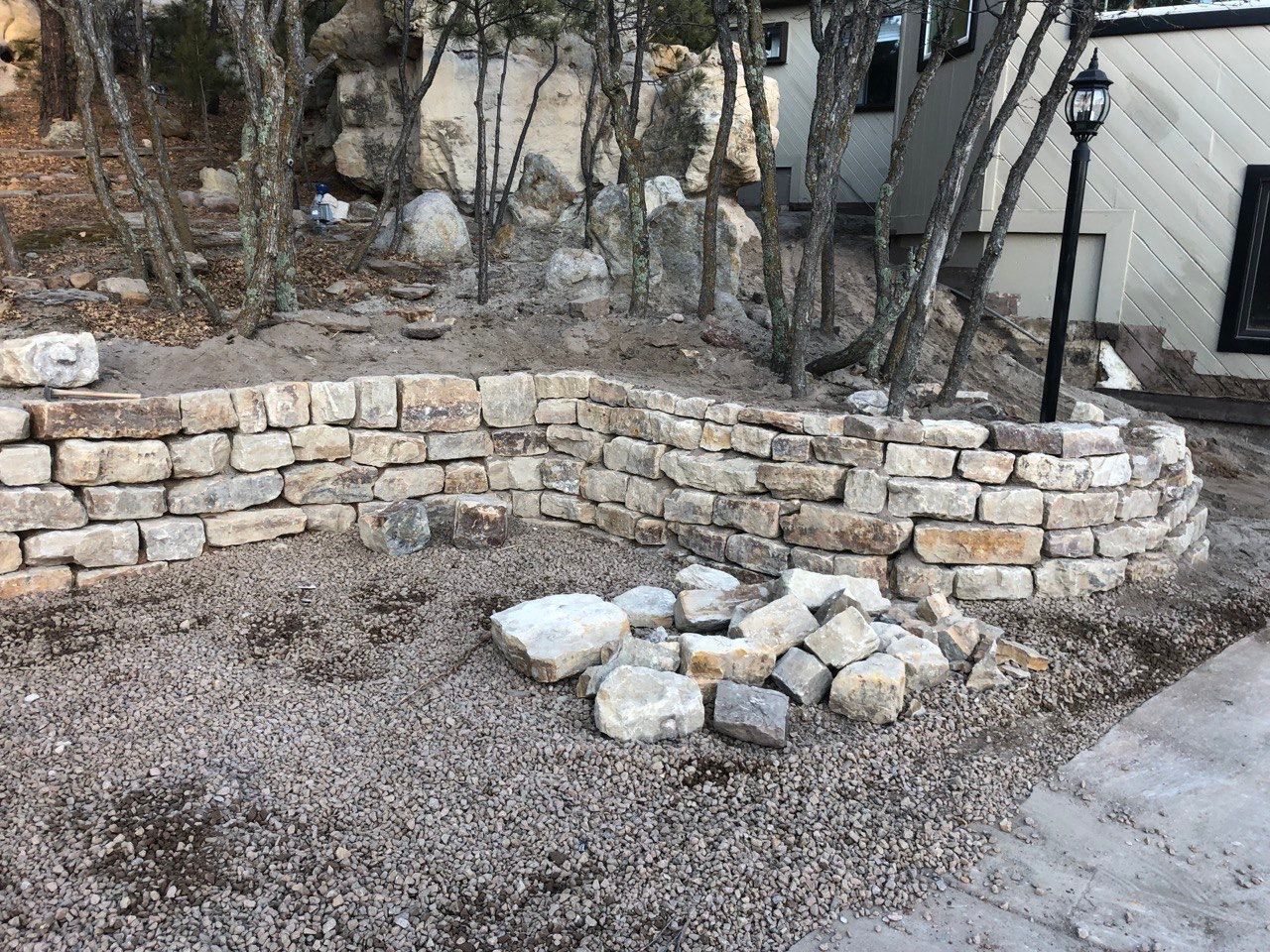 A stone wall is being built in the backyard of a house.