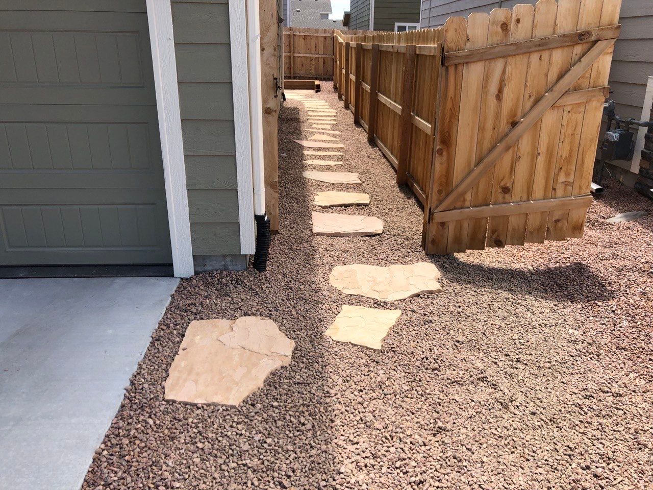A wooden fence surrounds a gravel path leading to a garage