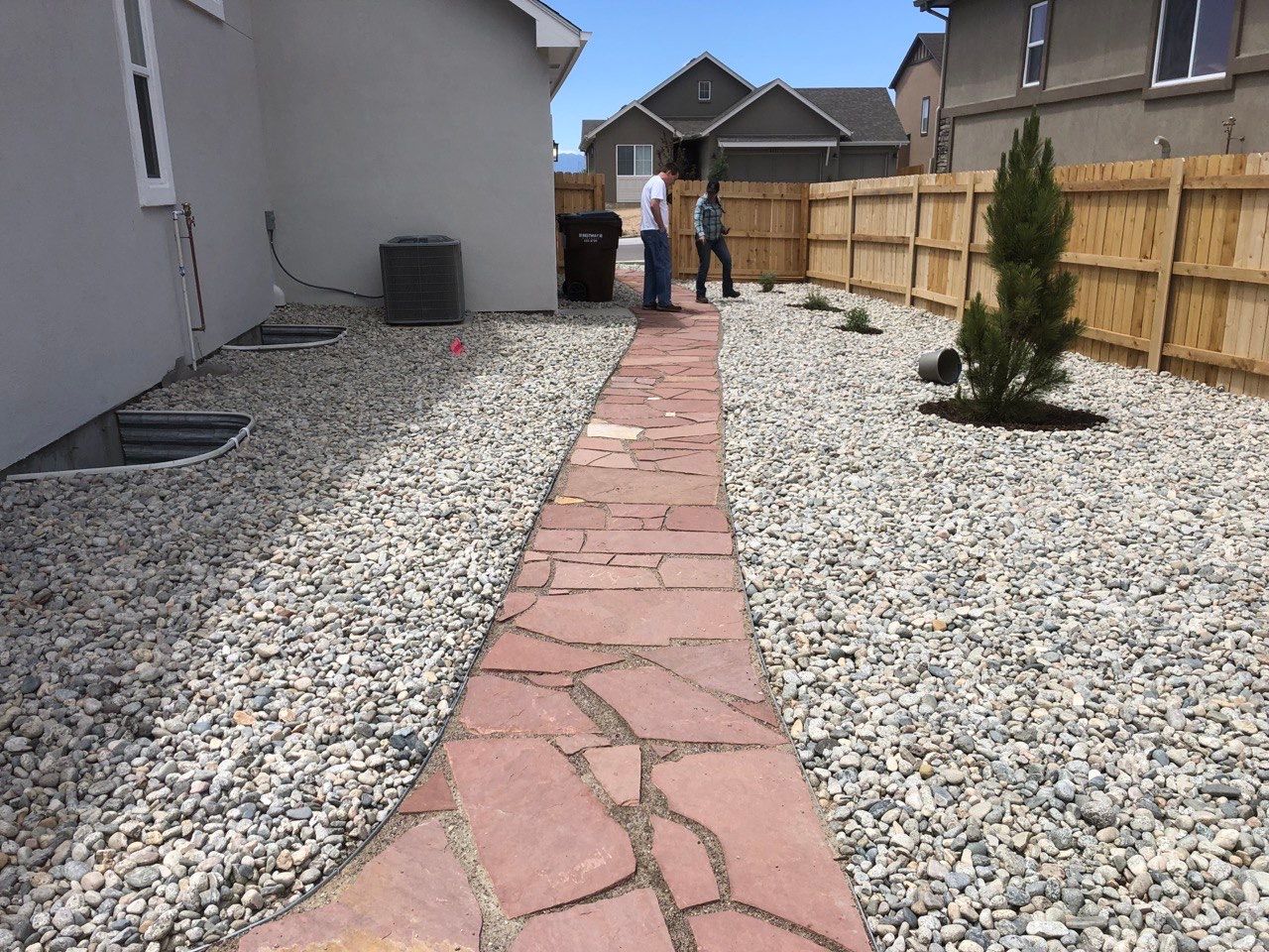 A stone walkway leads to a house with a wooden fence