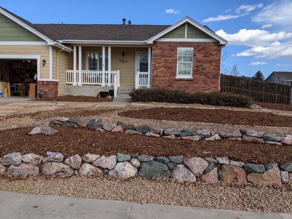 House with rock retaining walls, front porch, and garage. Landscaping features mulch and gravel.