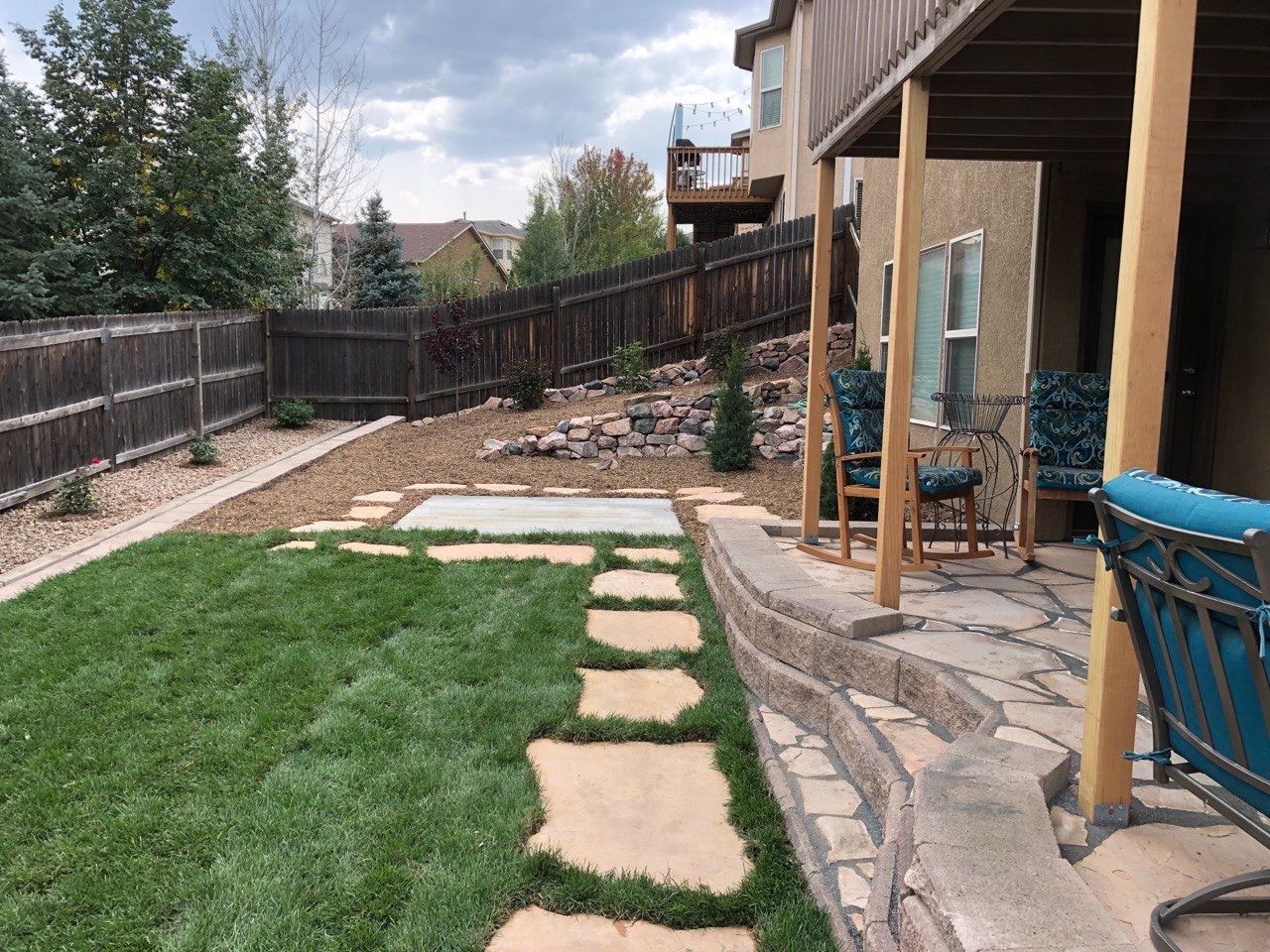 A backyard with a patio and rocking chairs and a fence
