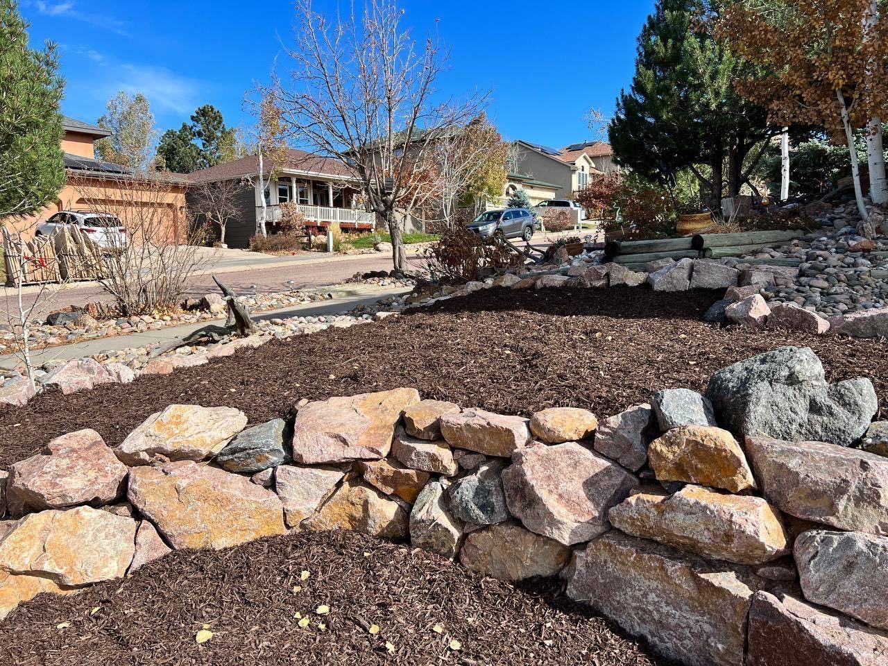 A pile of rocks in a garden with a house in the background.
