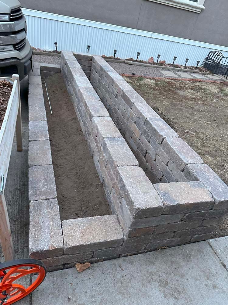 Two rectangular brick raised garden beds side-by-side on concrete, containing soil.