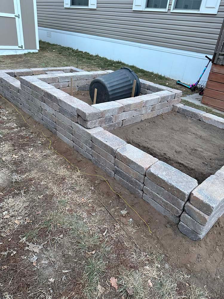 Raised garden beds constructed from brown pavers, with a dark container inside.