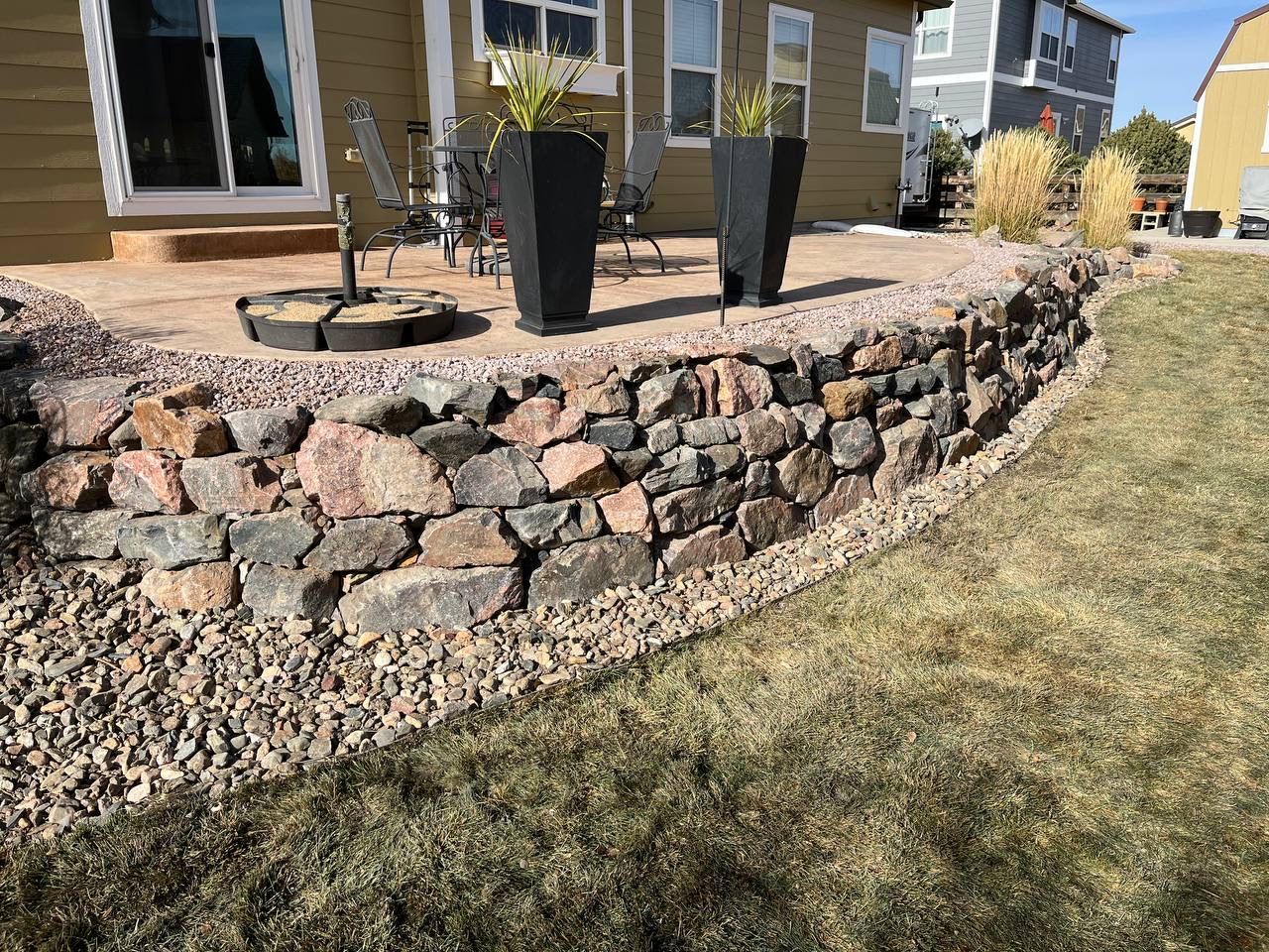 A stone wall surrounds a patio area in front of a house.