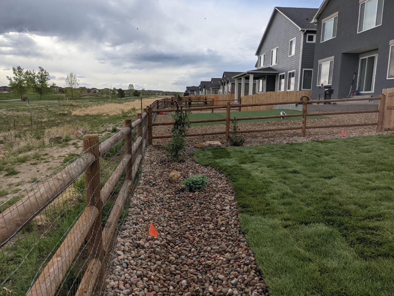 A wooden fence surrounds a lush green field with a house in the background.