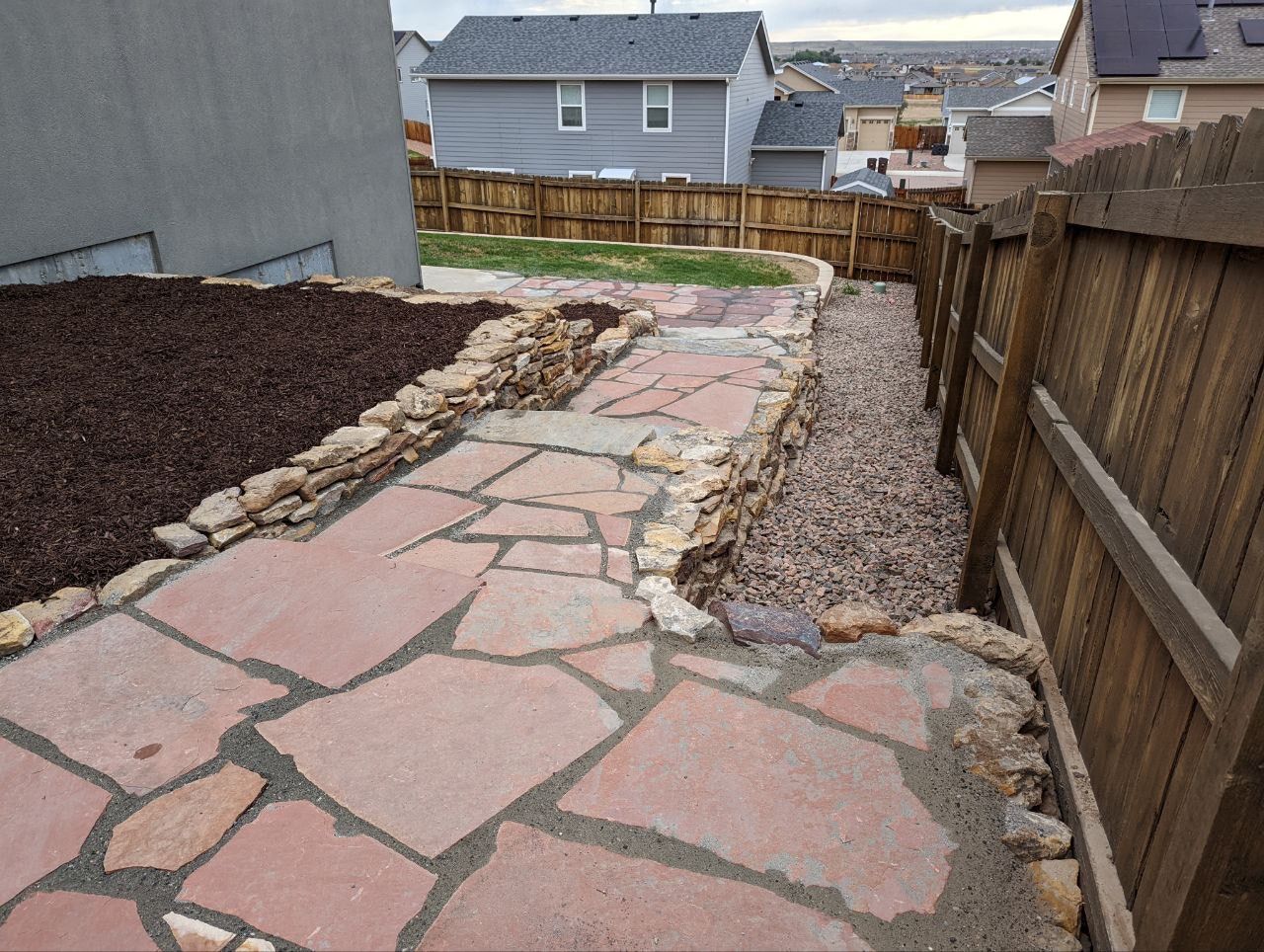 A stone walkway leading to a house with a wooden fence