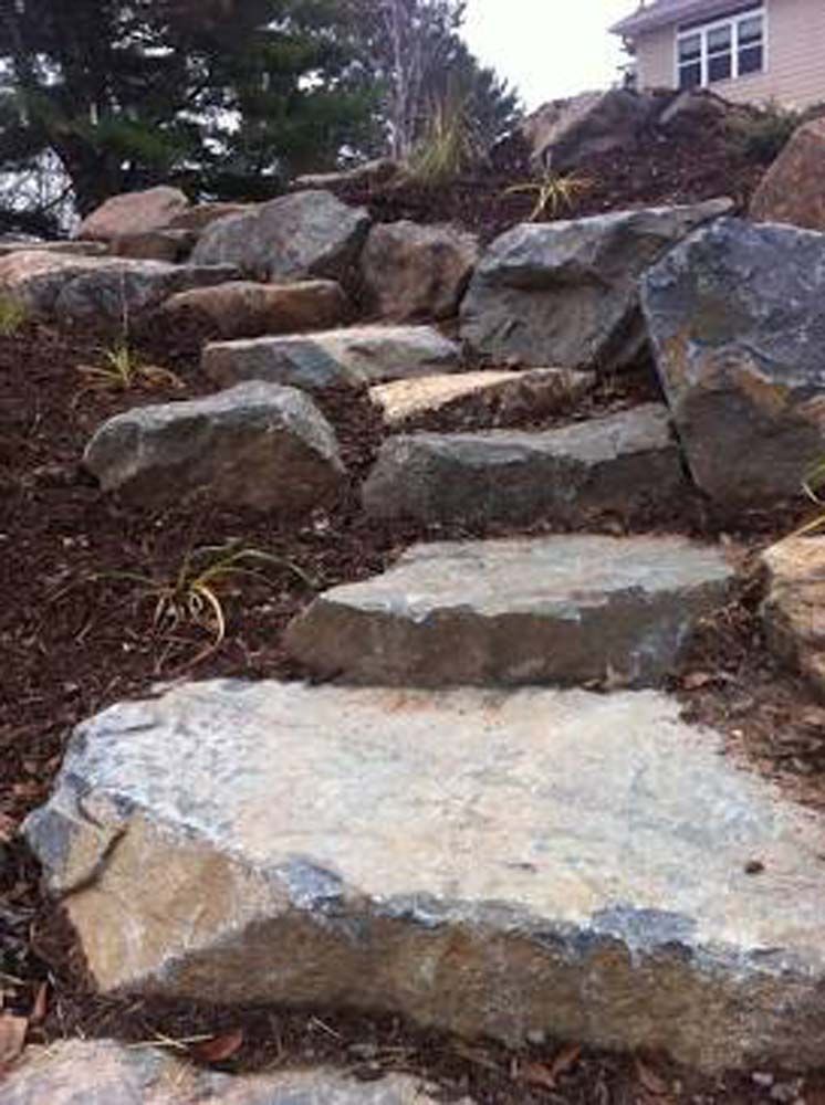 Stone steps ascending a hill with mulch and sparse vegetation.