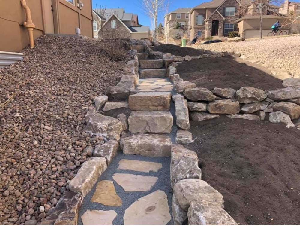 Stone staircase leading uphill through a landscaped yard with rocks and mulch.