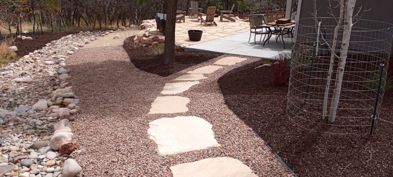 A stone walkway leading to a patio in a backyard