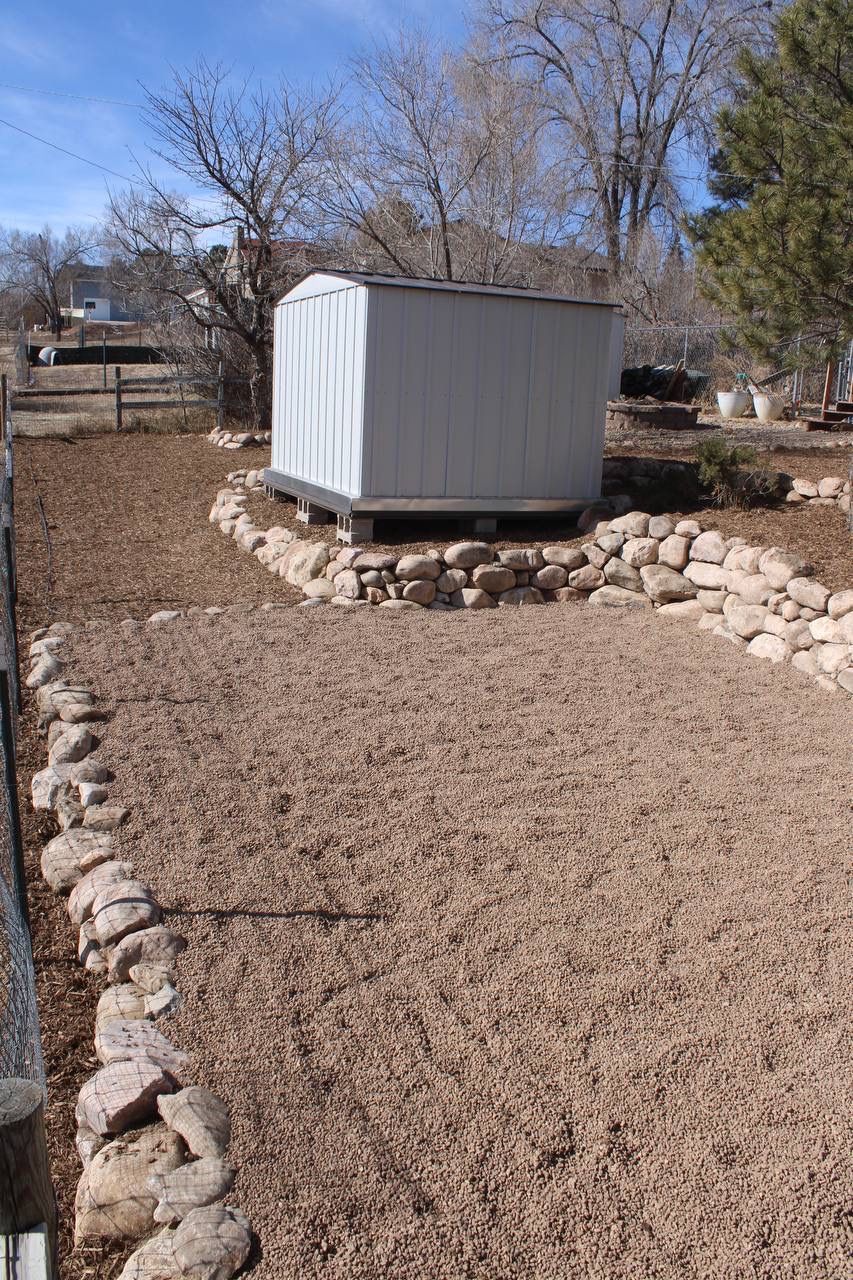 A white shed sits in the middle of a gravel yard