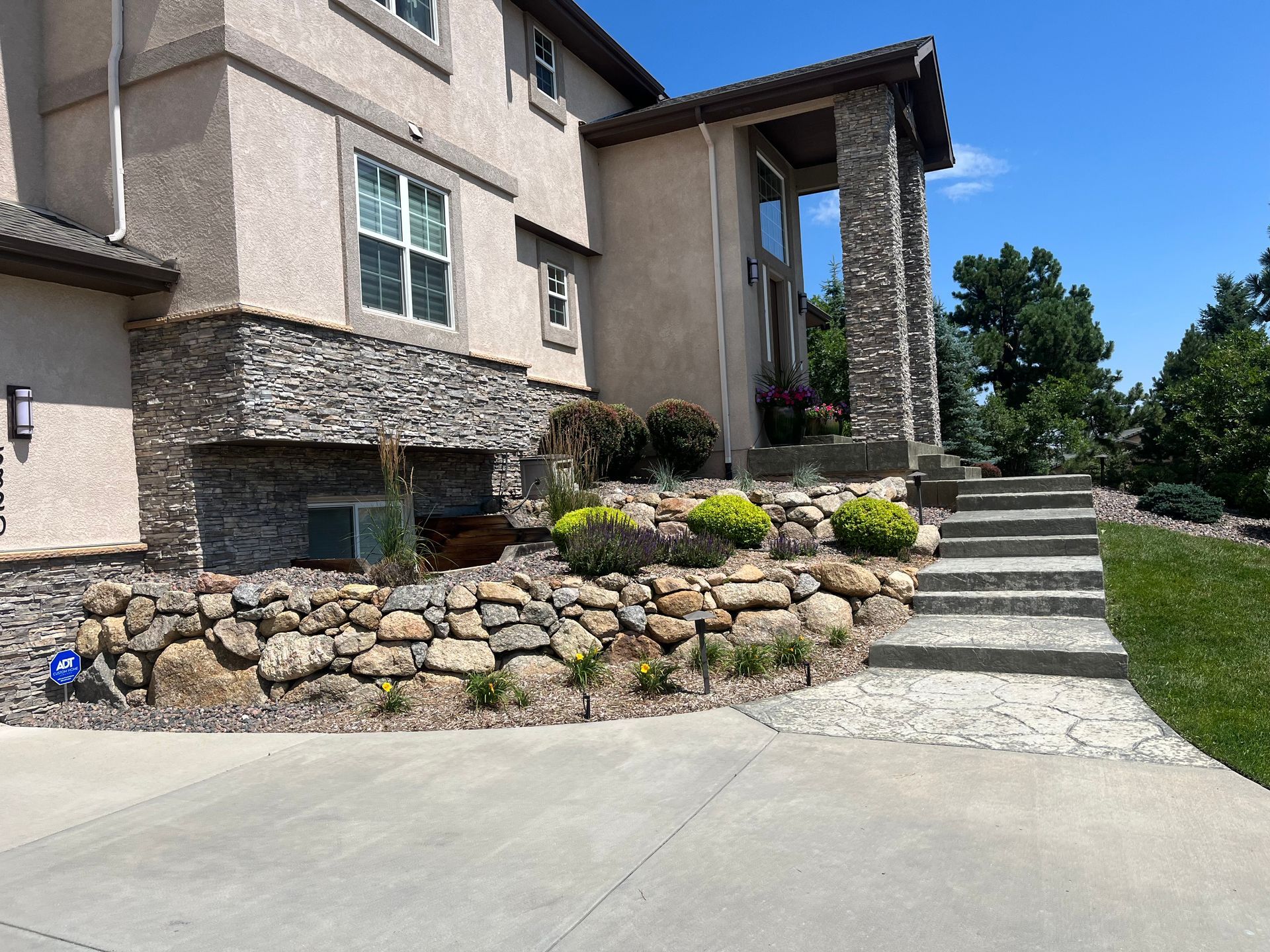 A beige stucco house with stone accents, rock retaining walls, and a concrete staircase leading to the entrance.