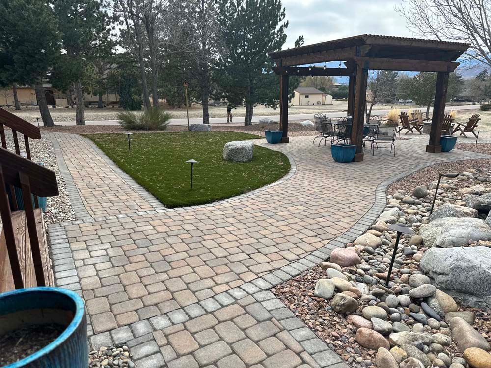 Brick pathway leads to pergola with seating, small lawn, and rock garden.
