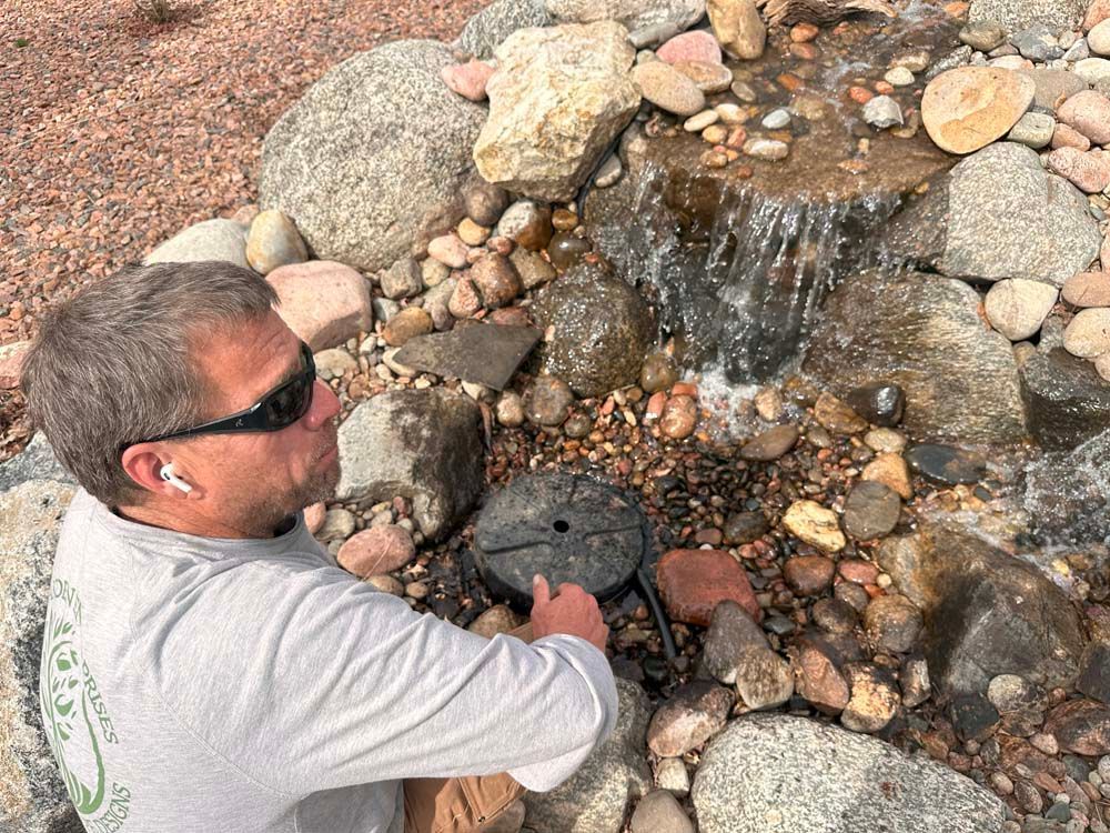 Man inspecting a small waterfall feature in a rock garden.