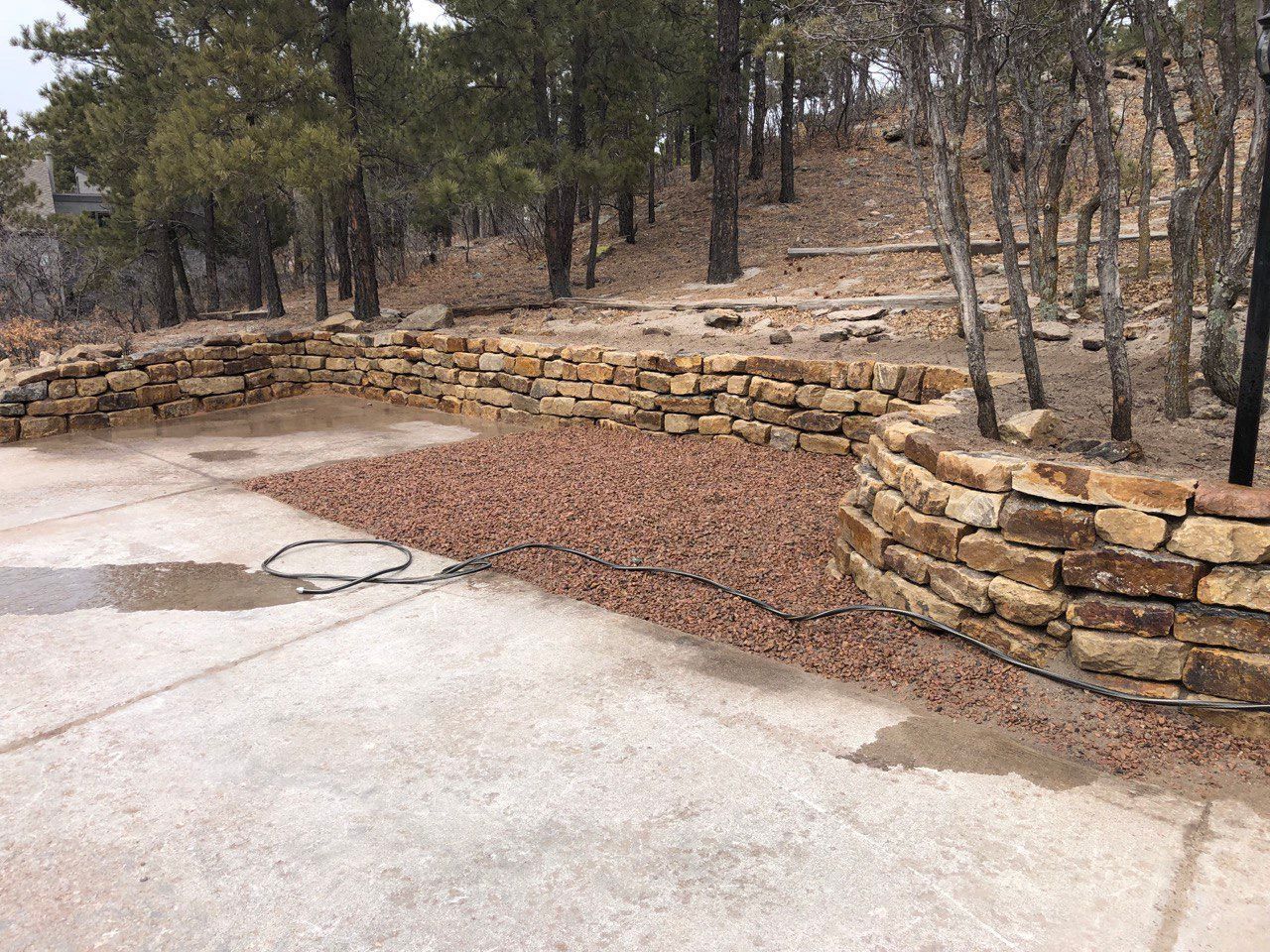 A stone wall surrounds a concrete driveway with trees in the background