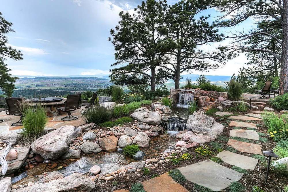 Stone path leads to a waterfall in a garden overlooking a city.