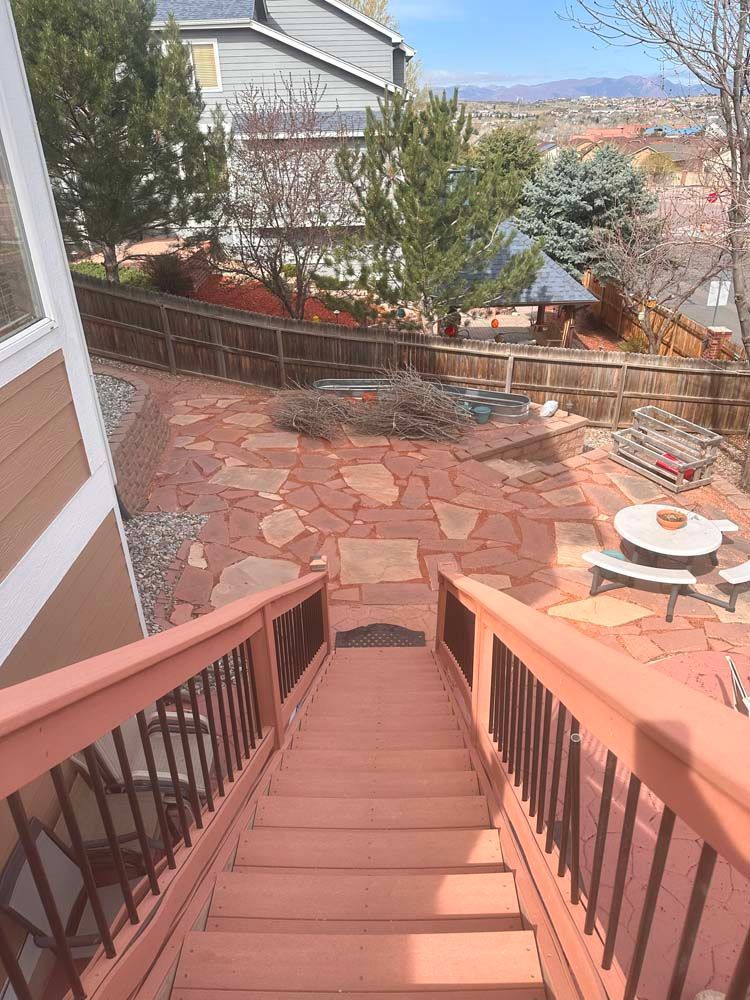 View down wooden stairs to a backyard patio with stone paving, gazebo, and distant mountains.
