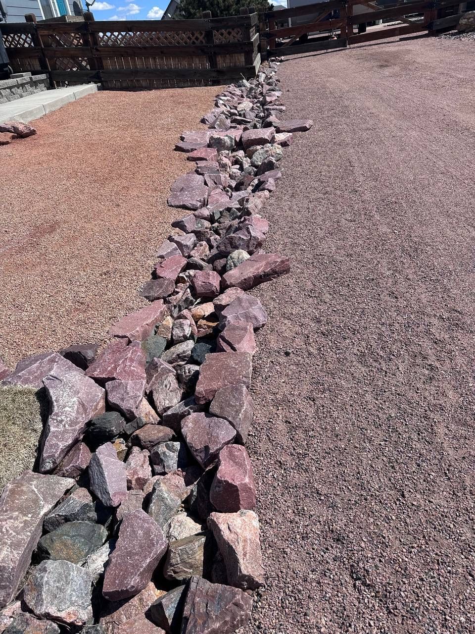 A row of rocks sitting on top of gravel next to a wooden fence.