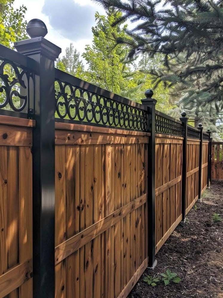 Wooden fence with black metal accents and decorative top, in a garden setting.