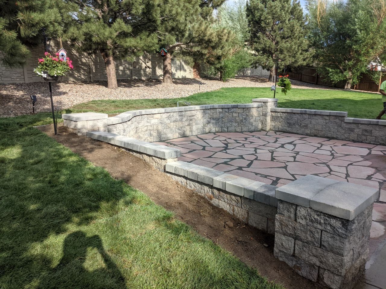 A stone wall is surrounded by grass and trees in a backyard.