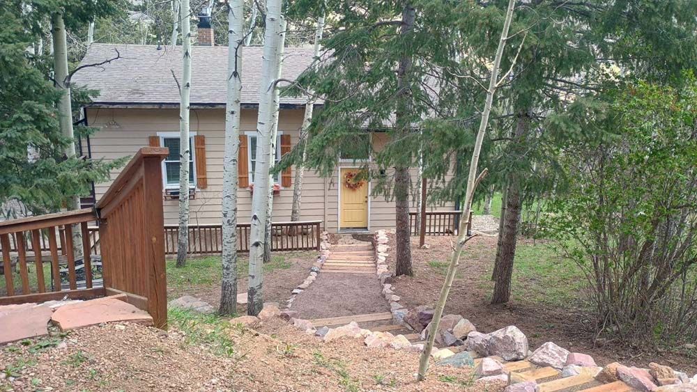 Small cabin with a path leading to the entrance, surrounded by trees and a wooden fence.