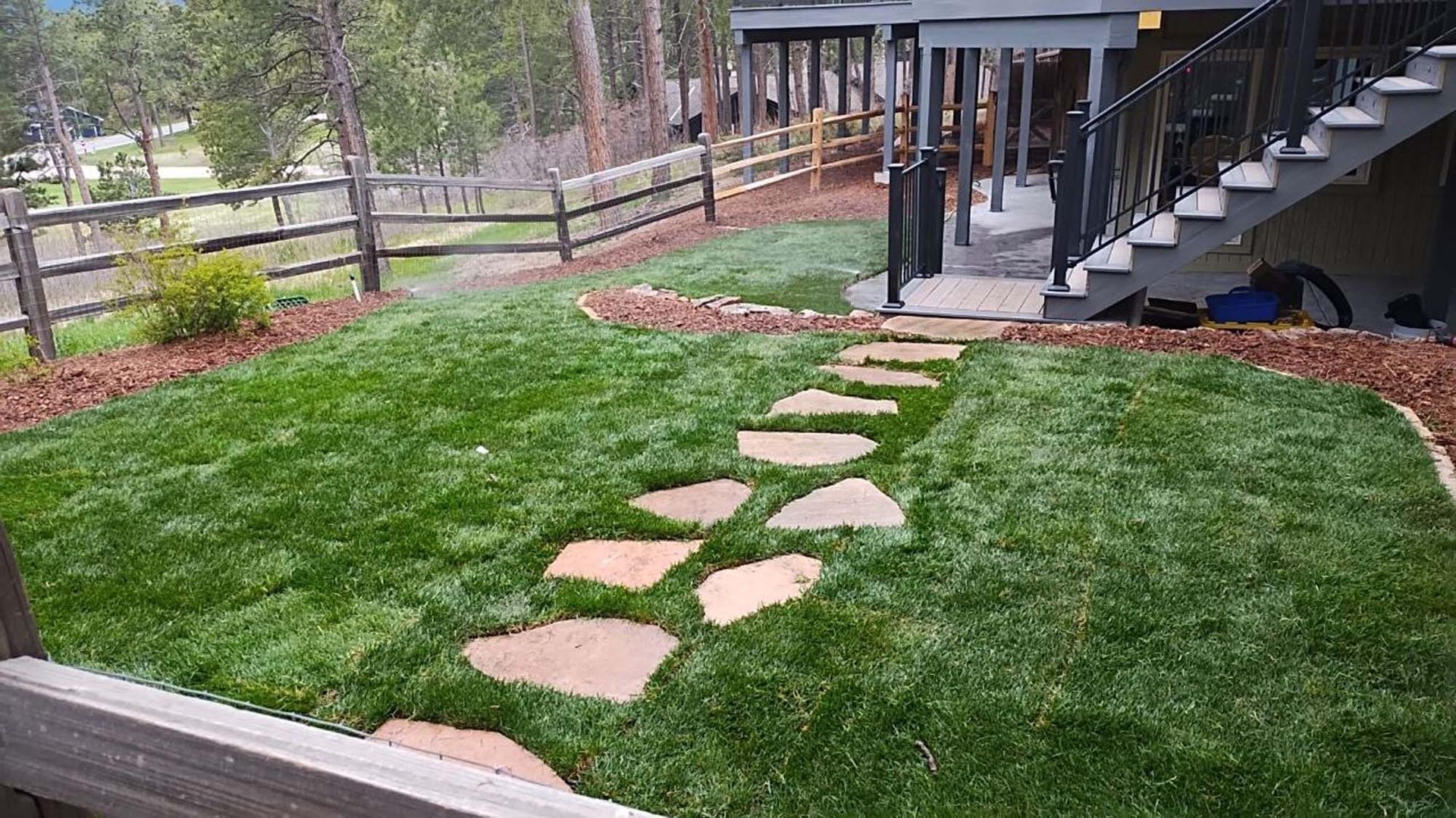 A lush green lawn with a stone walkway leading to a deck.