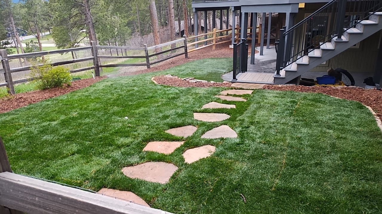 A lush green lawn with a stone walkway leading to a deck.