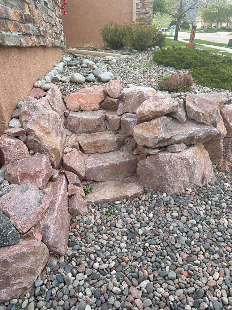 Stone steps leading up a rock retaining wall, with gravel and landscaping around them.