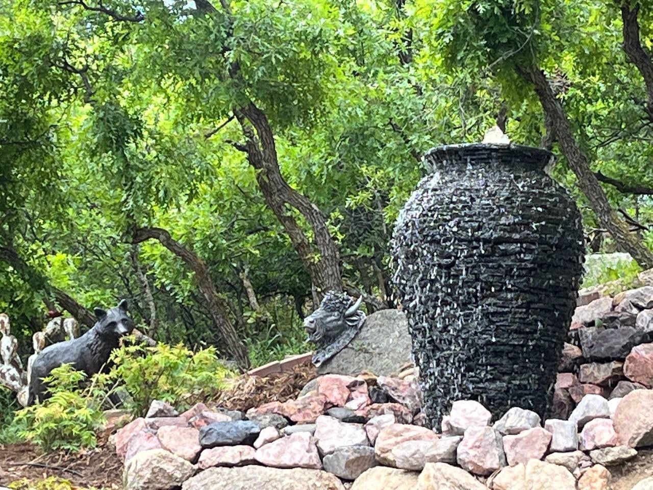 A large vase is sitting on top of a rocky hill in the middle of a forest.
